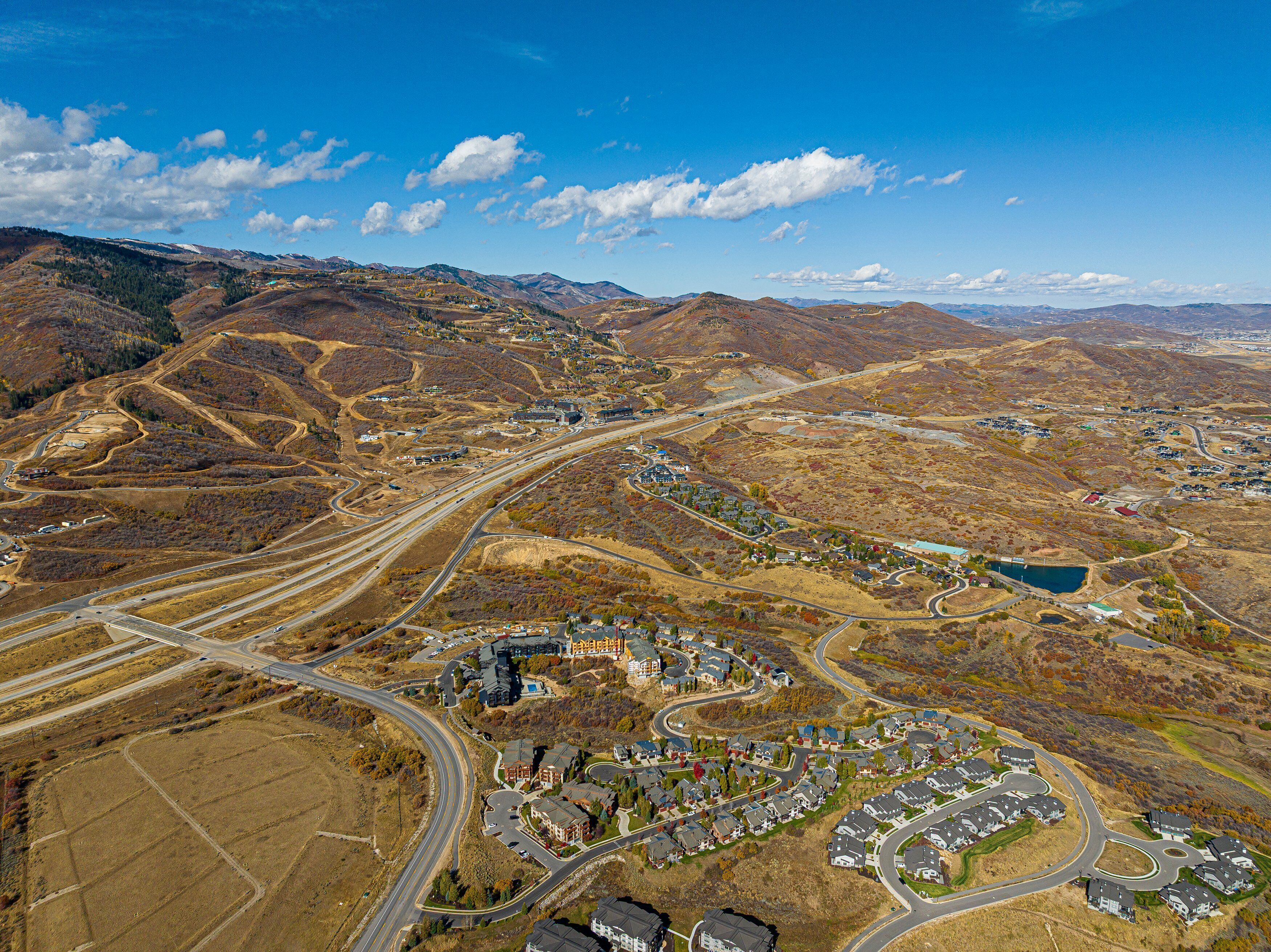 An aerial view of a residential area with winding roads, a small lake, and hilly terrain.