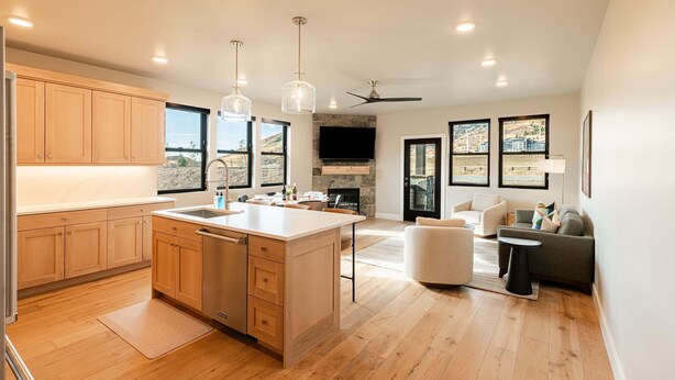 A modern kitchen with wooden cabinets, a central island, pendant lights, and a stone fireplace.