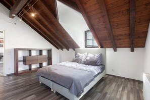 A bedroom with a sloped ceiling, a bed with a headboard, a bedside table, and a built-in bench.