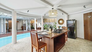 A spacious indoor area with a pool, a wooden bar, and a kitchen area. - Ombak Villa by Kozystay - Canggu (Canggu)
