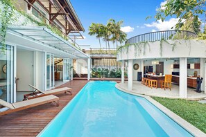 A swimming pool with lounge chairs, a covered patio, and a modern kitchen area. - Ombak Villa by Kozystay - Canggu (Canggu)