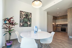 Un espace repas moderne avec une table ronde, des chaises blanches, une plante en pot et une œuvre d’art accrochée au mur.
