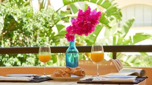 A breakfast setup with croissants, orange juice, and a blue vase with pink flowers on a balcony with a view of greenery. - Beach and Golf Design Apartment Marbella (Marbella)