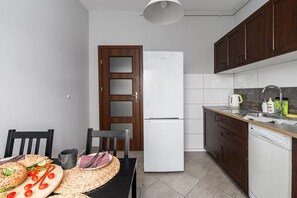 Eine kleine Küche mit einem weißen Kühlschrank, Holzschränken und einem Essbereich mit Tisch für zwei Personen.