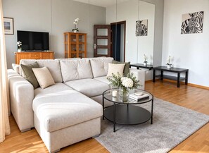 Ein modernes Wohnzimmer mit einer Eckcouch, einem Glastisch und Kunstwerken an den Wänden.