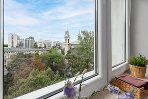 Blick aus einem Fenster auf eine Stadtlandschaft mit modernen Gebäuden und einer Kirche mit hohem Turm.