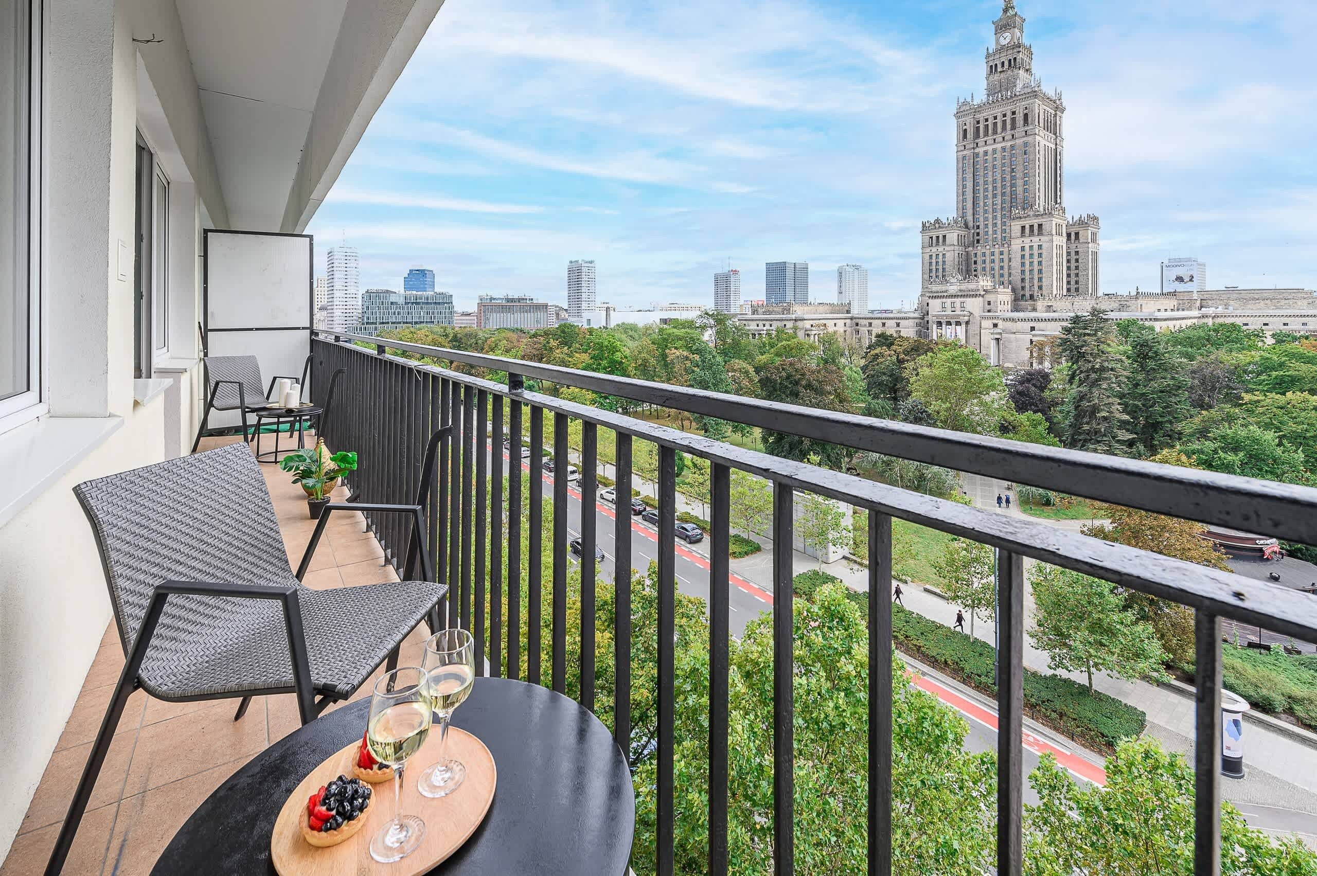 A balcony with a table set for two, overlooking a cityscape with a prominent building.