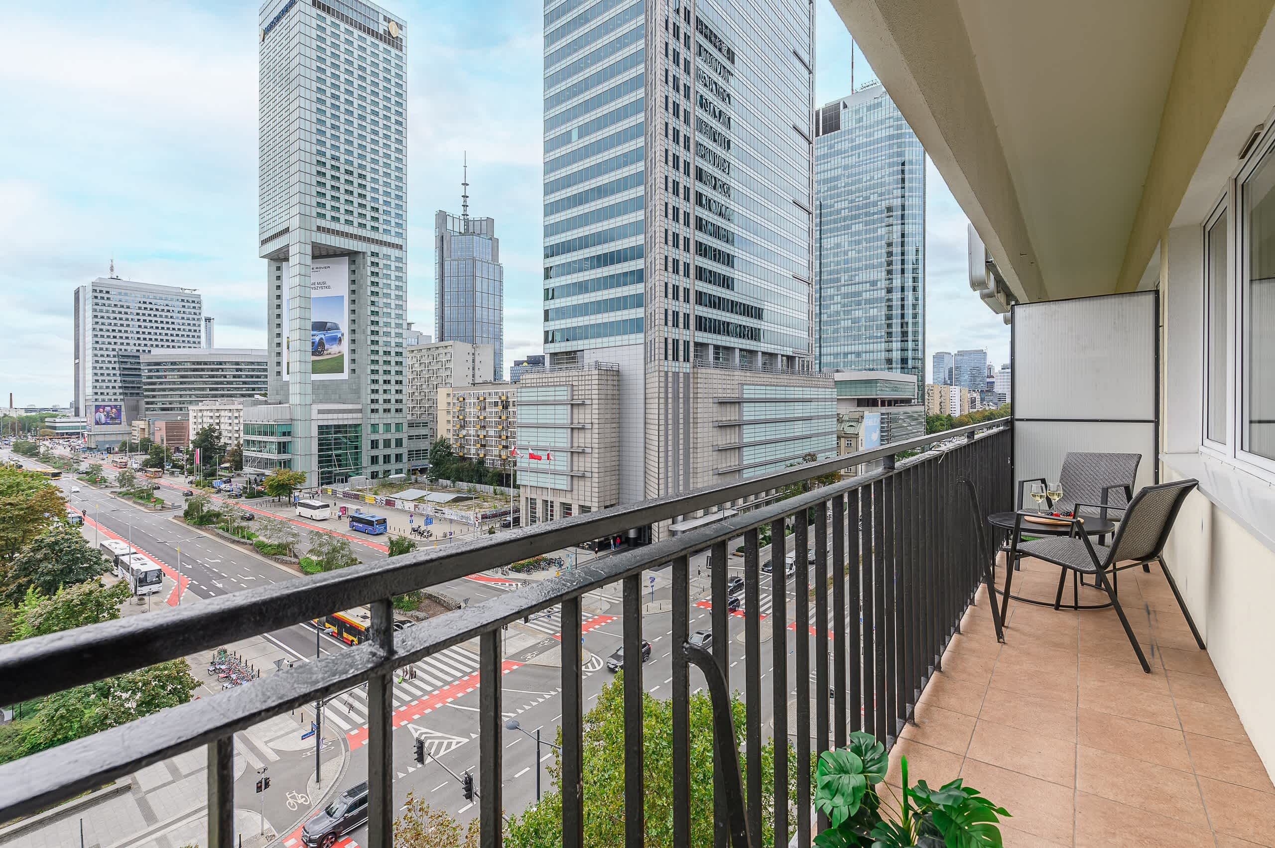 A balcony with a view of a cityscape, including tall buildings and a busy street.