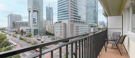 Un balcón con vistas a un paisaje urbano, que incluye edificios altos y una calle concurrida.