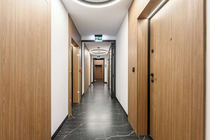 A modern hotel corridor with wooden doors, black marble flooring, and recessed lighting.
