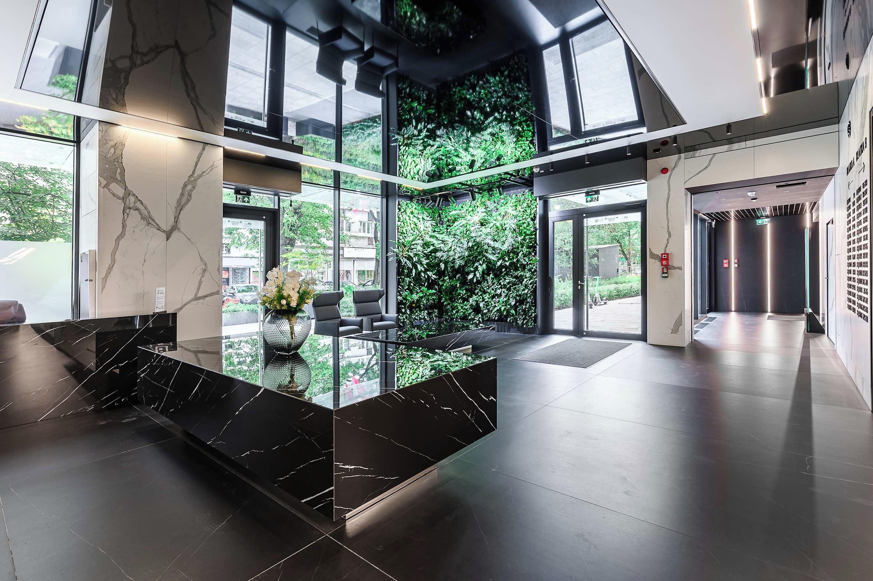 Un moderno vestíbulo con una recepción de mármol, ventanas amplias y una pared verde.
