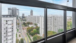 A high-rise building with multiple floors, large windows, and a view of a cityscape with other buildings and a road. - 2-Room Apart on 15th Floor (Warszawa)