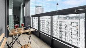 A balcony with a wooden table, two glasses of red wine, and a bowl of grapes. - 2-Room Apart on 15th Floor (Warszawa)