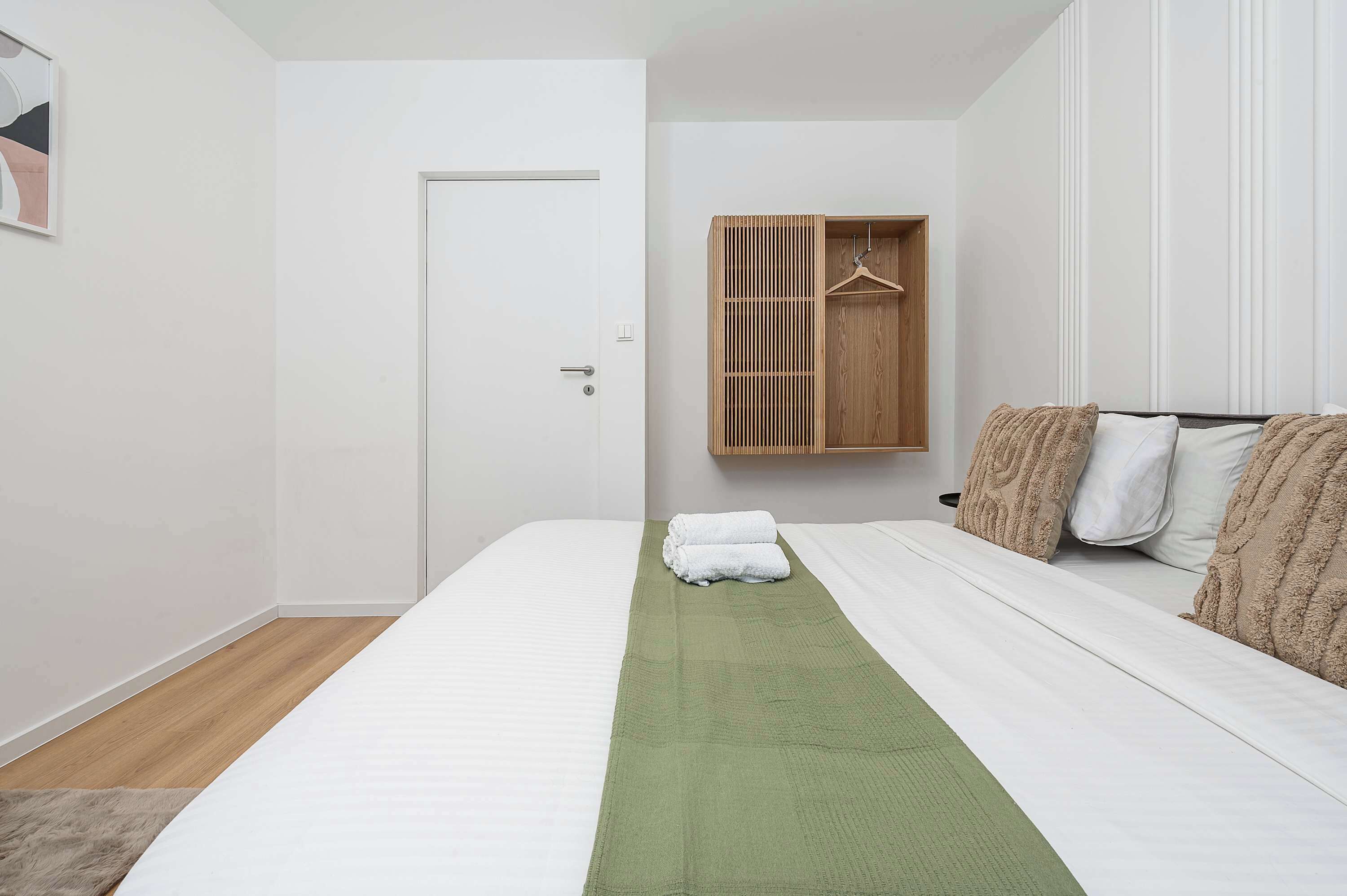Ein Schlafzimmer mit einem Bett, einer grünen Tagesdecke, einem Holzschrank mit Kleiderhaken und einer Tür.