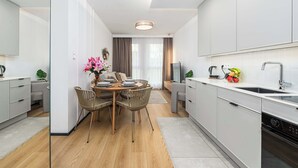 Eine moderne Küche mit weißen Schränken, ein Essbereich mit Holztisch und Korbstühlen sowie ein großes Fenster mit Vorhängen.