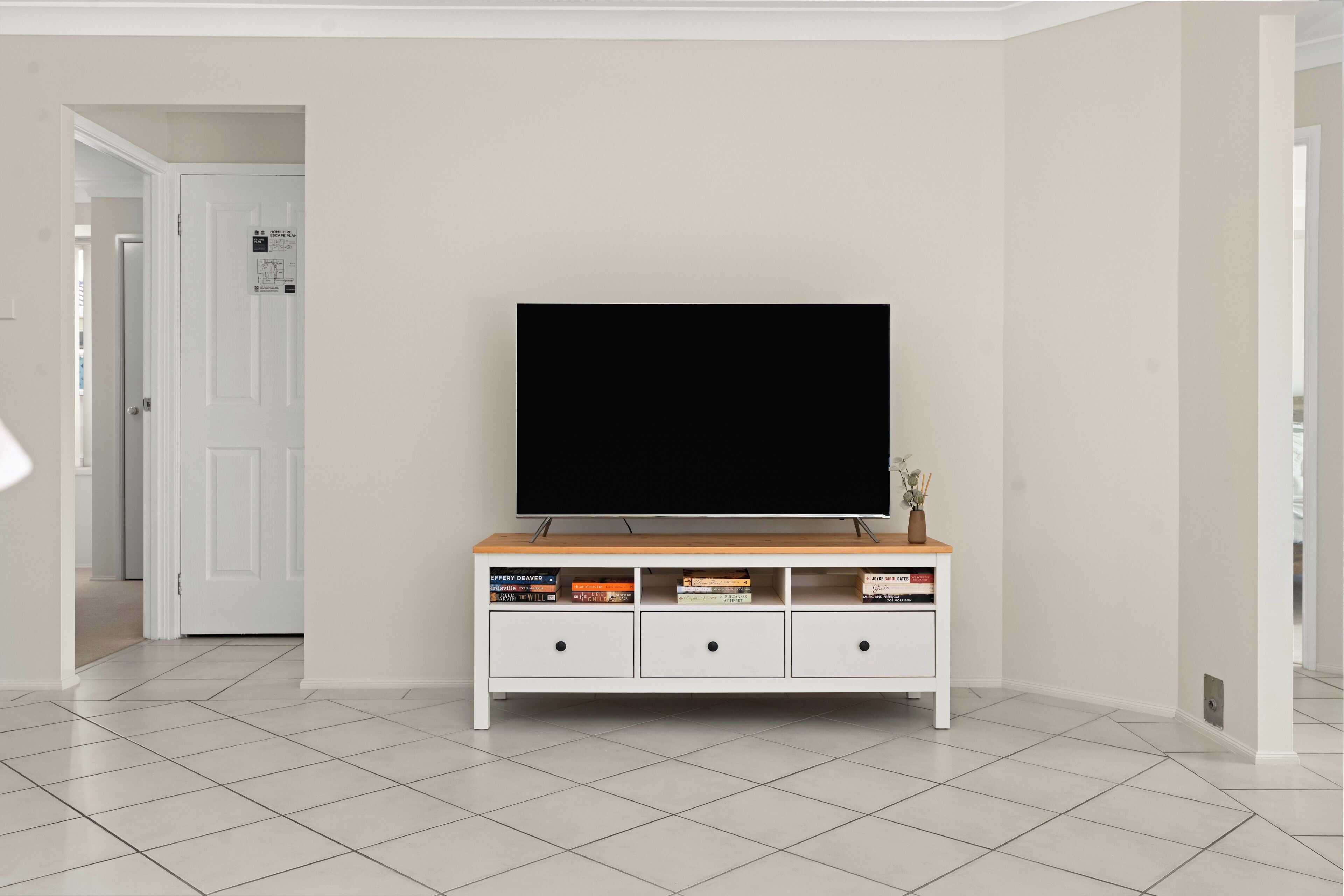 A living room with a flat-screen TV on a wooden TV stand, a white door, and a tiled floor.