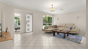 A spacious living room with a beige sofa, a wooden coffee table, and a patterned rug. - 3 minute drive to the beach! Family home with a BBQ, boardgames, and a backyard. (Callala Bay)
