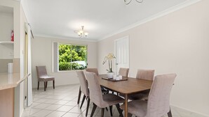 A dining area with a wooden table, six chairs, and a vase of flowers. - 3 minute drive to the beach! Family home with a BBQ, boardgames, and a backyard. (Callala Bay)