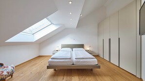 Een moderne slaapkamer met dakraam, een bed met twee kussens, nachtkastjes met lampen en ingebouwde kasten.