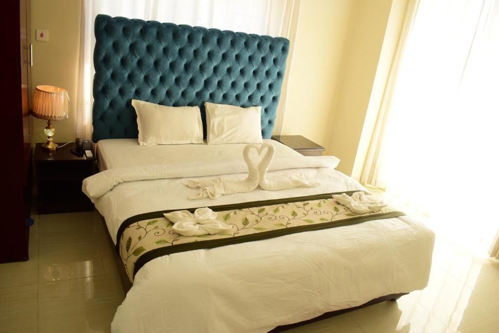 A neatly made bed with a tufted headboard, a bedside lamp, and a tray with towels.