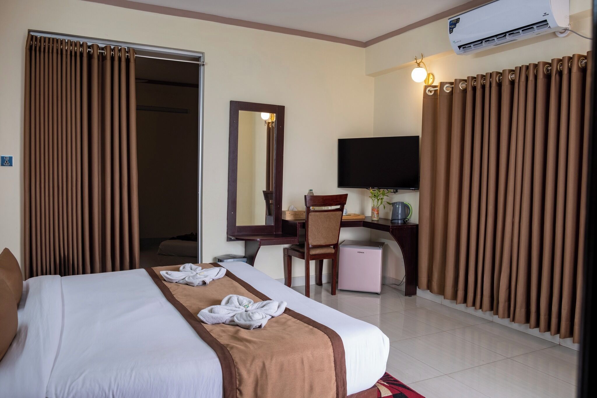 A hotel room with a bed, a desk, a chair, a television, and an air conditioning unit.