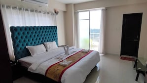 A hotel room with a large bed, a flat-screen TV, a window with curtains, and a door. - Hotel Beach Park (Cox's Bazar)
