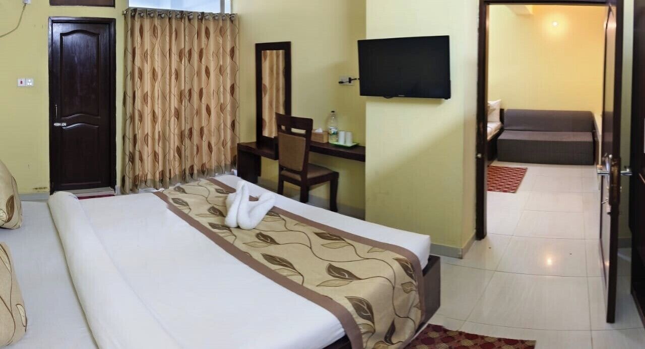 Una habitación de hotel con cama, escritorio, sillón, televisión y sofá en la sala contigua.