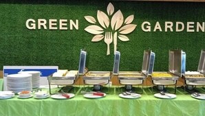 A buffet setup with multiple food stations, plates, and utensils on a green tablecloth, with a backdrop featuring the words "GREEN GARDEN". - Hotel Beach Park (Cox's Bazar)