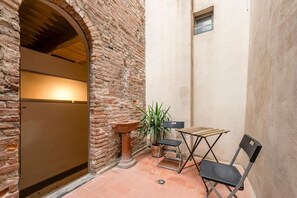 Un mur de briques, une porte, une petite table avec des chaises et une plante en pot.