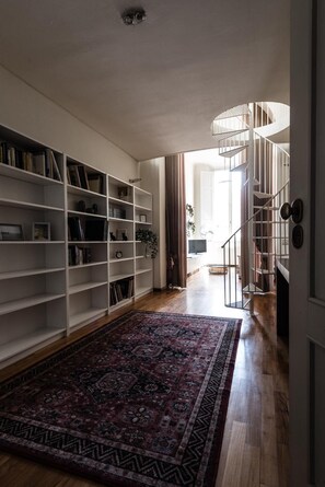 Ein geräumiger Flur mit einem großen, gemusterten Teppich, einem Bücherregal und einer Wendeltreppe.