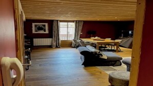 A cozy room with a wooden ceiling, a dining table, a sofa, and a small rug.