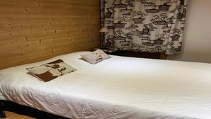 A single bed with a white duvet and two pillows, a wooden headboard, and a curtain with a traditional pattern.