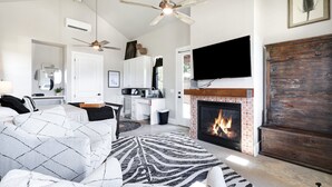 Amplia sala de estar con chimenea, ventilador de techo y televisión montada en la pared.