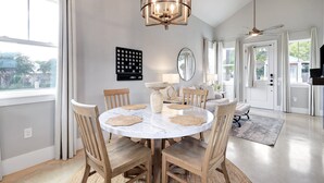 Ein Essbereich mit einem runden Tisch, Holzstühlen, einer Chandelier und Blick ins Freie.