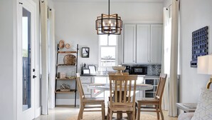 Eine moderne Küche mit weißen Schränken, einem Holztisch mit Stühlen und einer Pendelleuchte.