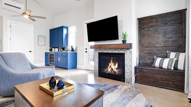 A living room with a fireplace, a television mounted above it, a sofa, and a coffee table with decorative items. - Frio - A Birdy Vacation Rental (Fredericksburg)