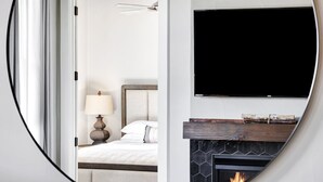 A bedroom with a bed, a bedside lamp, a TV mounted above a fireplace.