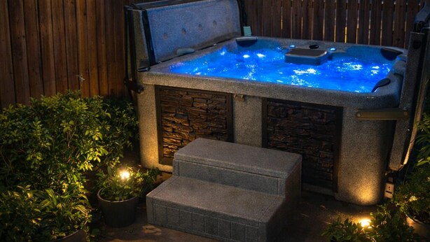 A hot tub with a stone exterior and a wooden fence in the background.