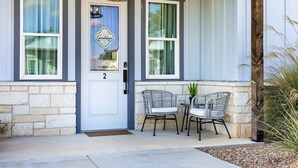 A house with a front door labeled "2", two wicker chairs, a small table, and a potted plant on the porch.