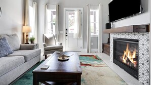 Ein Wohnzimmer mit Kamin, Sofa, Couchtisch und Wandfernseher.
