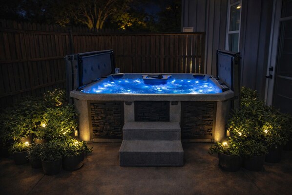 A hot tub with stone walls and a wooden deck, surrounded by potted plants and a wooden fence.