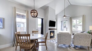 A spacious living room with a fireplace, a dining area with wooden chairs, and a large window with curtains.