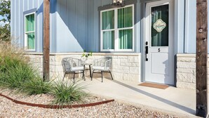 A building with a white door marked with the number 5, a porch with two wicker chairs, and a stone wall.
