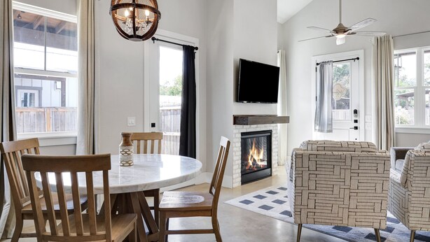 A modern living room with a fireplace, a round dining table with chairs, and a television mounted on the wall.