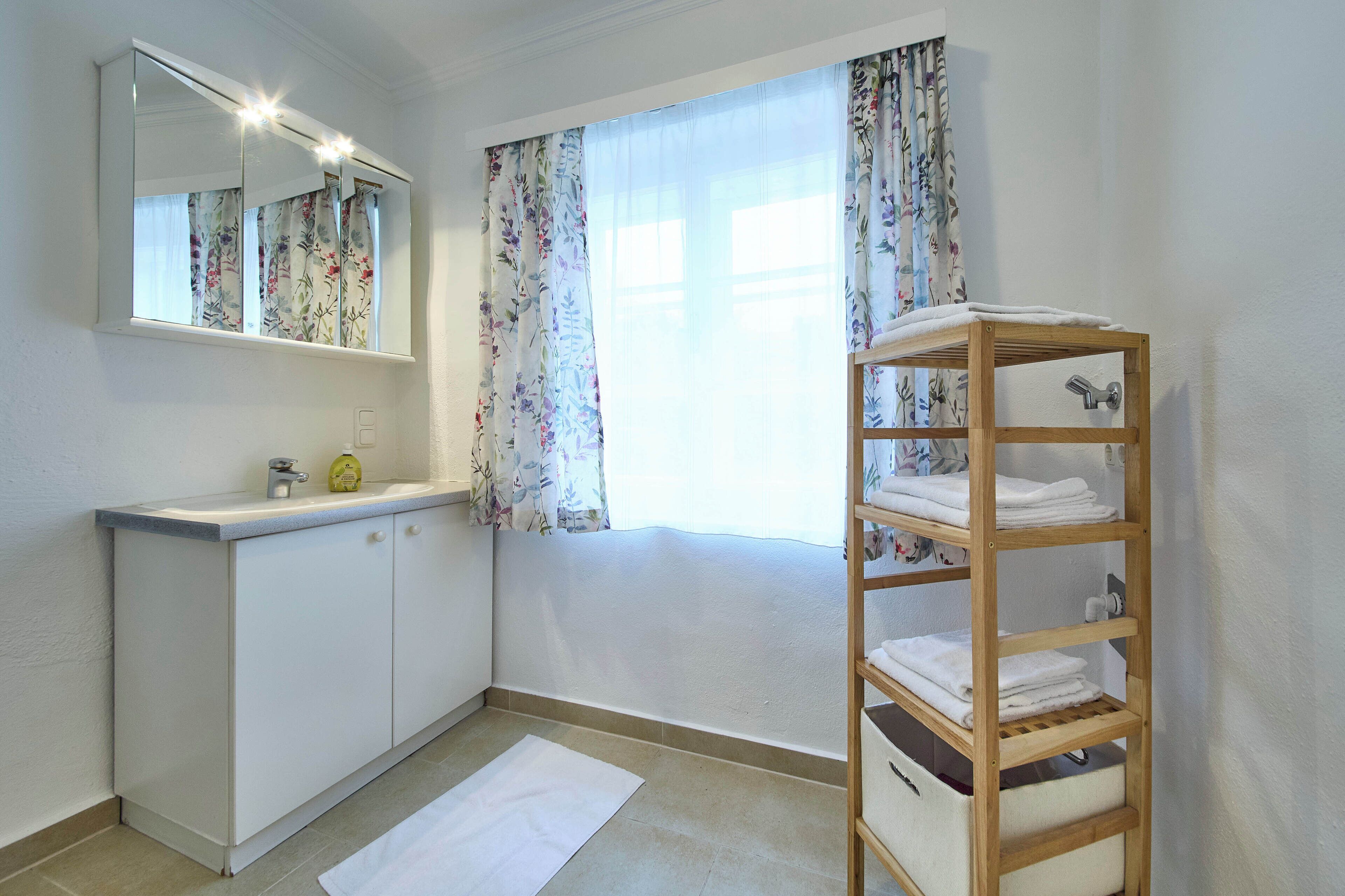 Un baño con lavamanos blanco, espejo y toallero de madera.