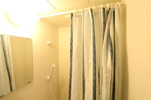 Une salle de bain avec un rideau de douche, un miroir et une douchette à main.