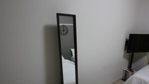 Une chambre à coucher avec un lit, une table de chevet, une lampe et un miroir qui reflète une horloge.