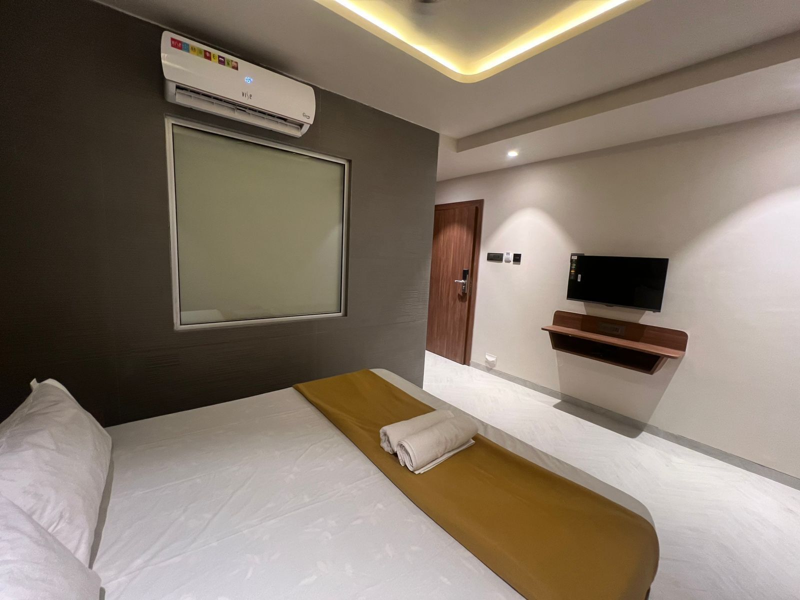 Une chambre d’hôtel équipée d’un lit, d’un téléviseur fixé au mur, d’une table de chevet en bois et d’un appareil de climatisation.
