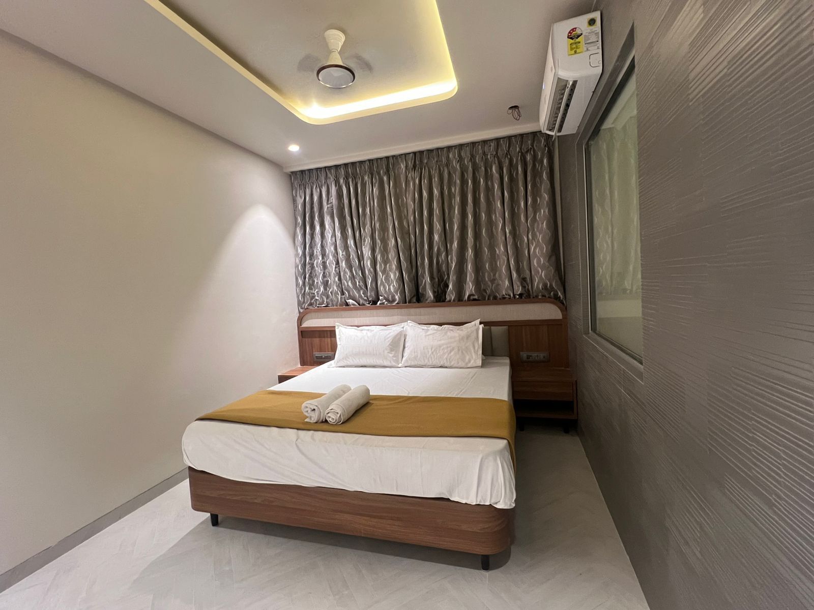 Une chambre d’hôtel moderne avec un lit en bois, du linge de lit blanc, un luminaire au plafond et un appareil de climatisation.