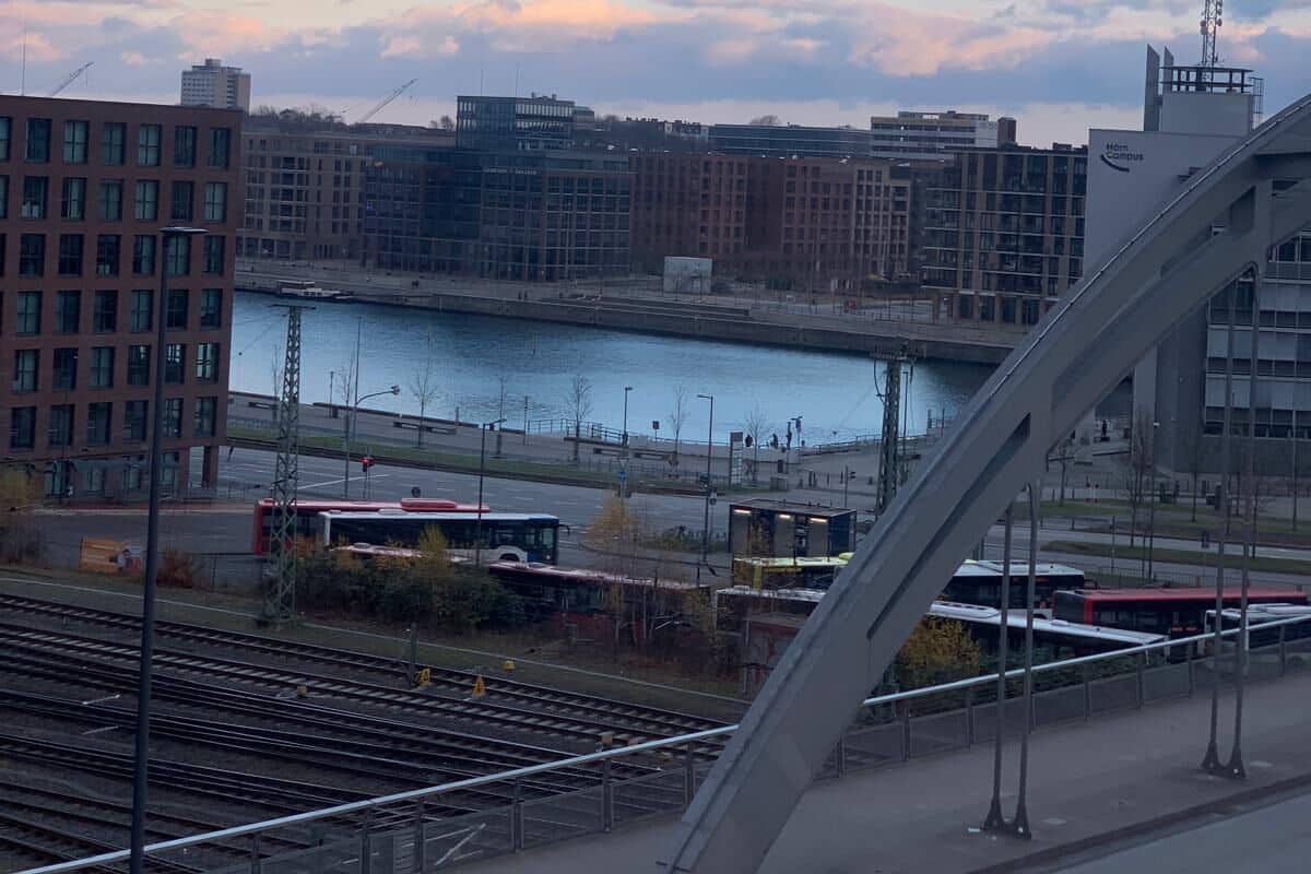 Blick auf einen Fluss mit modernen Gebäuden, einer Brücke und einer Straßenbahnlinie.